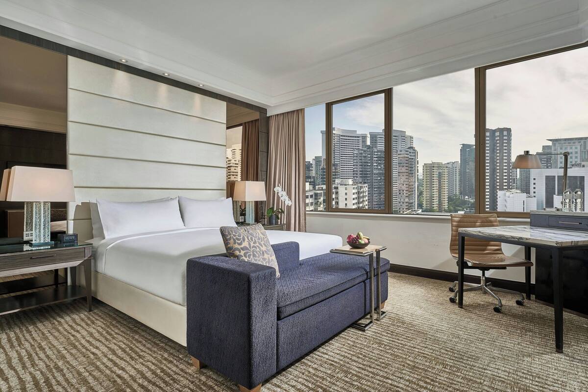 A hotel room with a bed, a sofa, a desk, and a view of the city skyline.