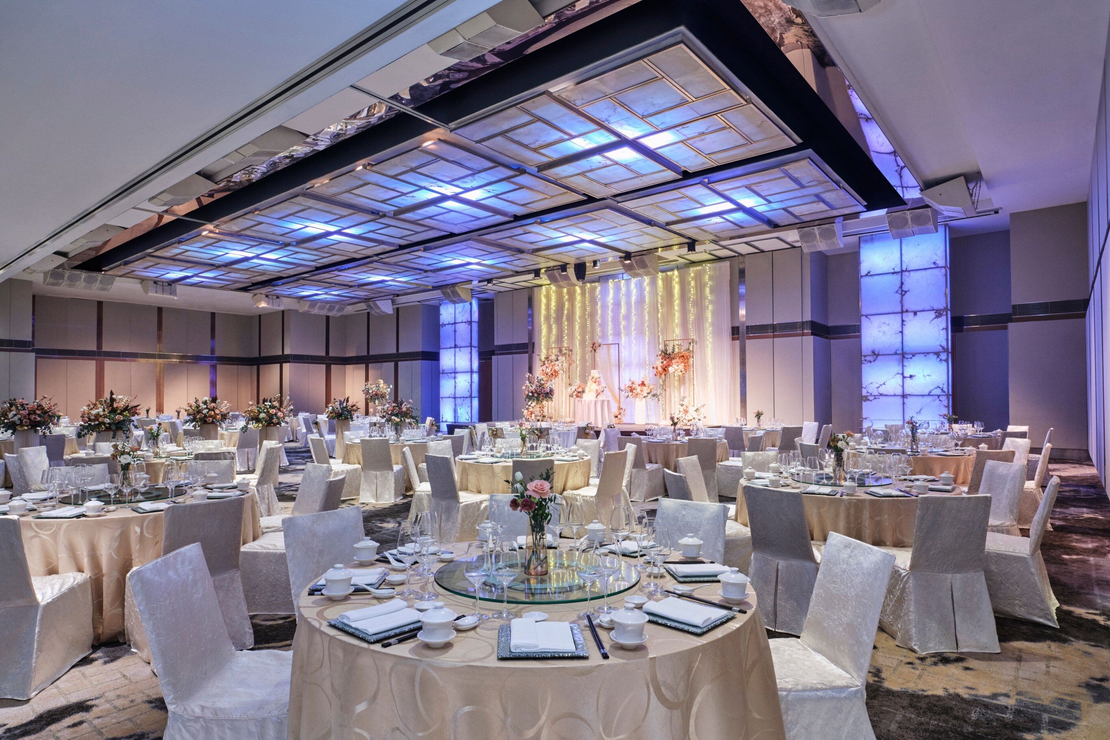 Une salle de banquet avec des tables rondes, des chaises blanches et des centres de table floraux.