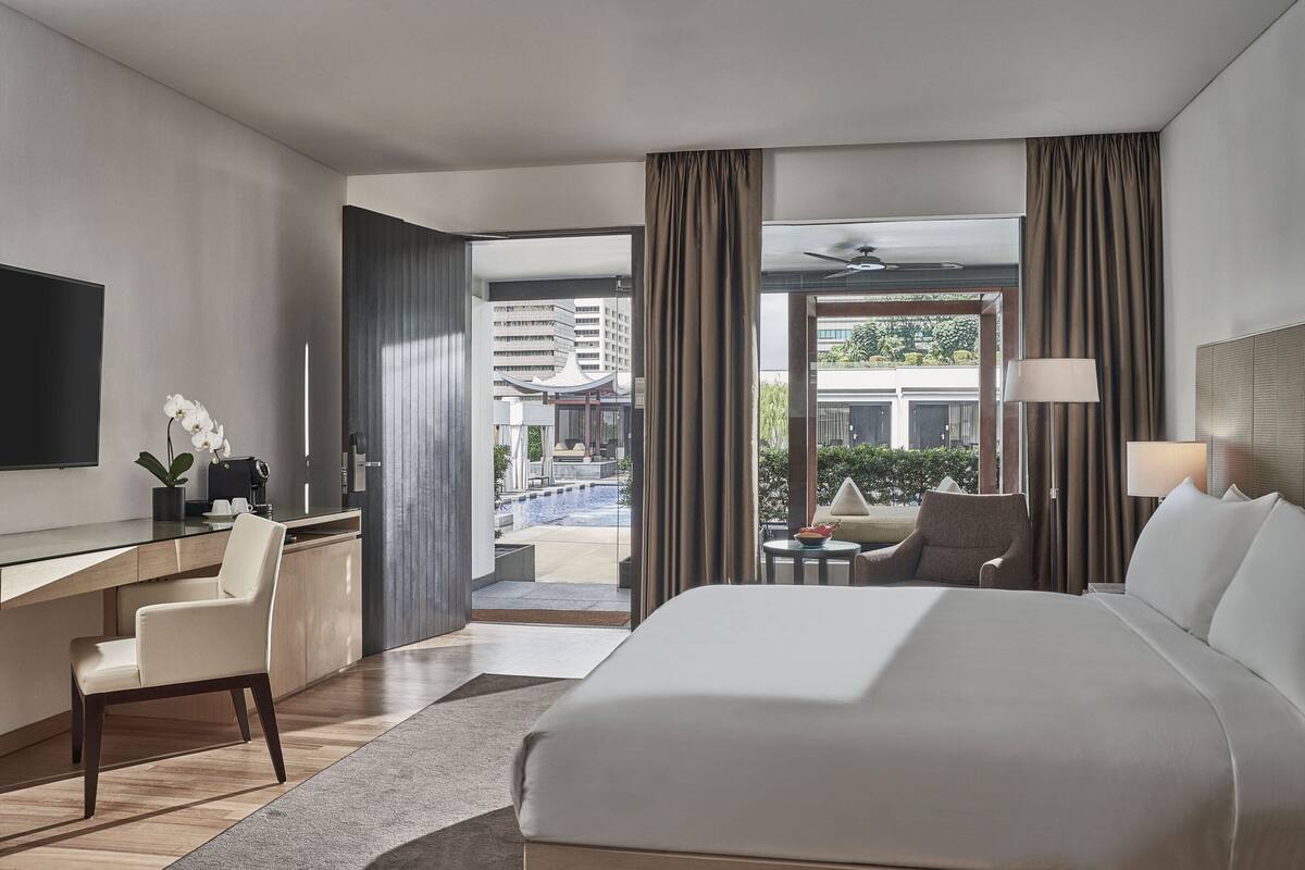 A hotel room with a bed, a desk, a chair, a TV, and a view of the outside.