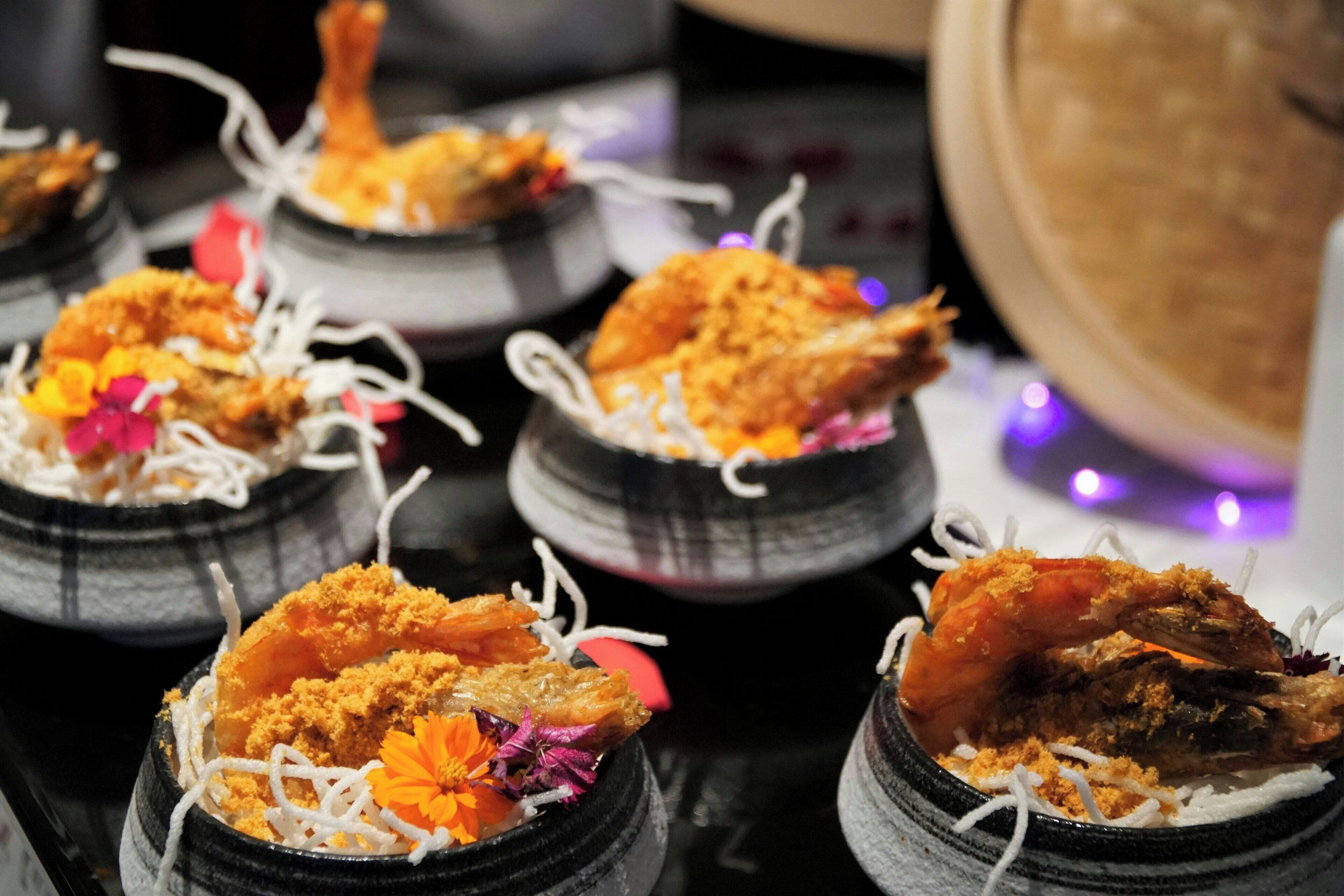 A series of dishes with seafood, garnished with flowers and white strands, presented in black bowls.
