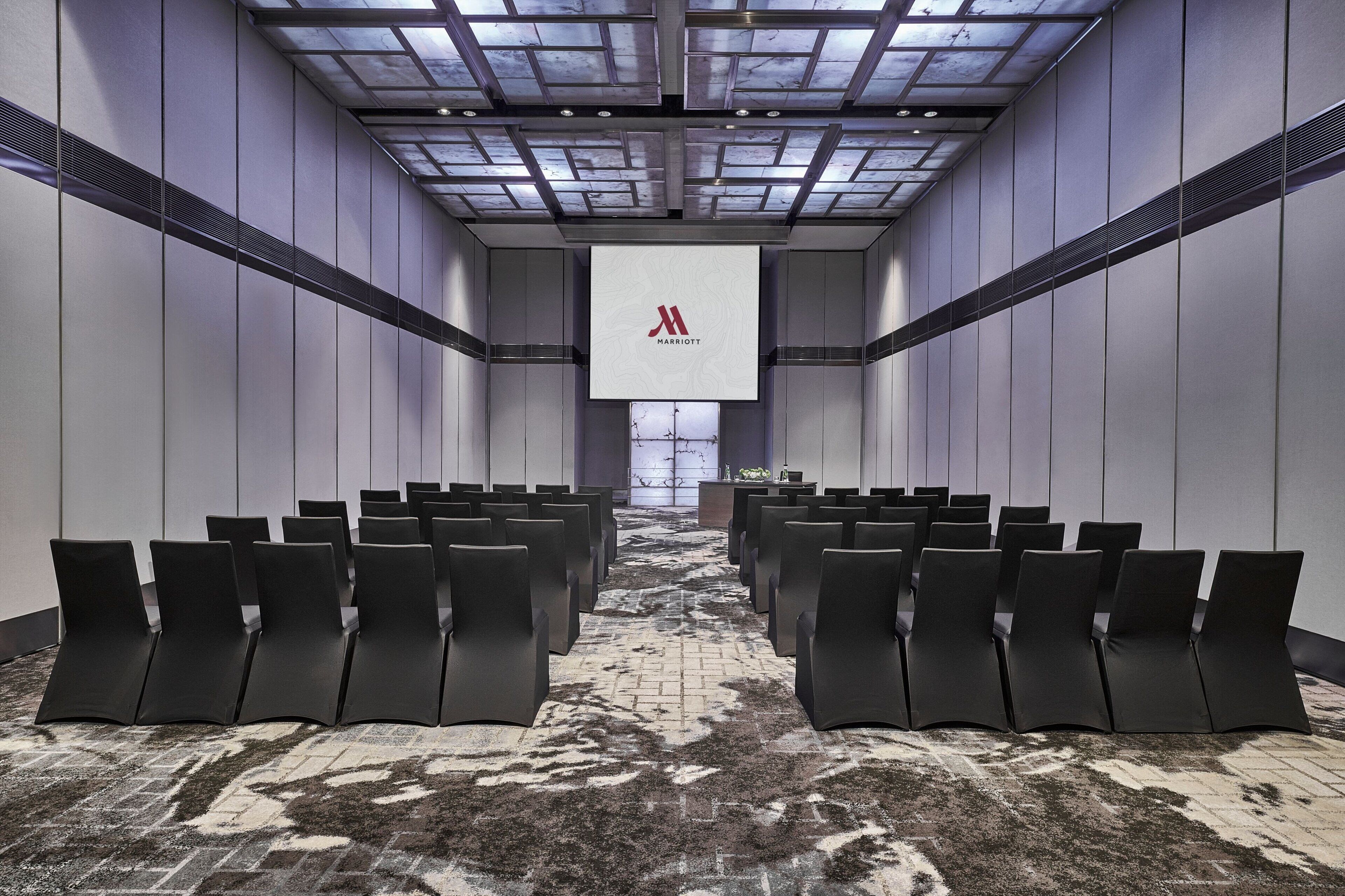 A conference room with rows of black chairs facing a large screen displaying the Marriott logo.