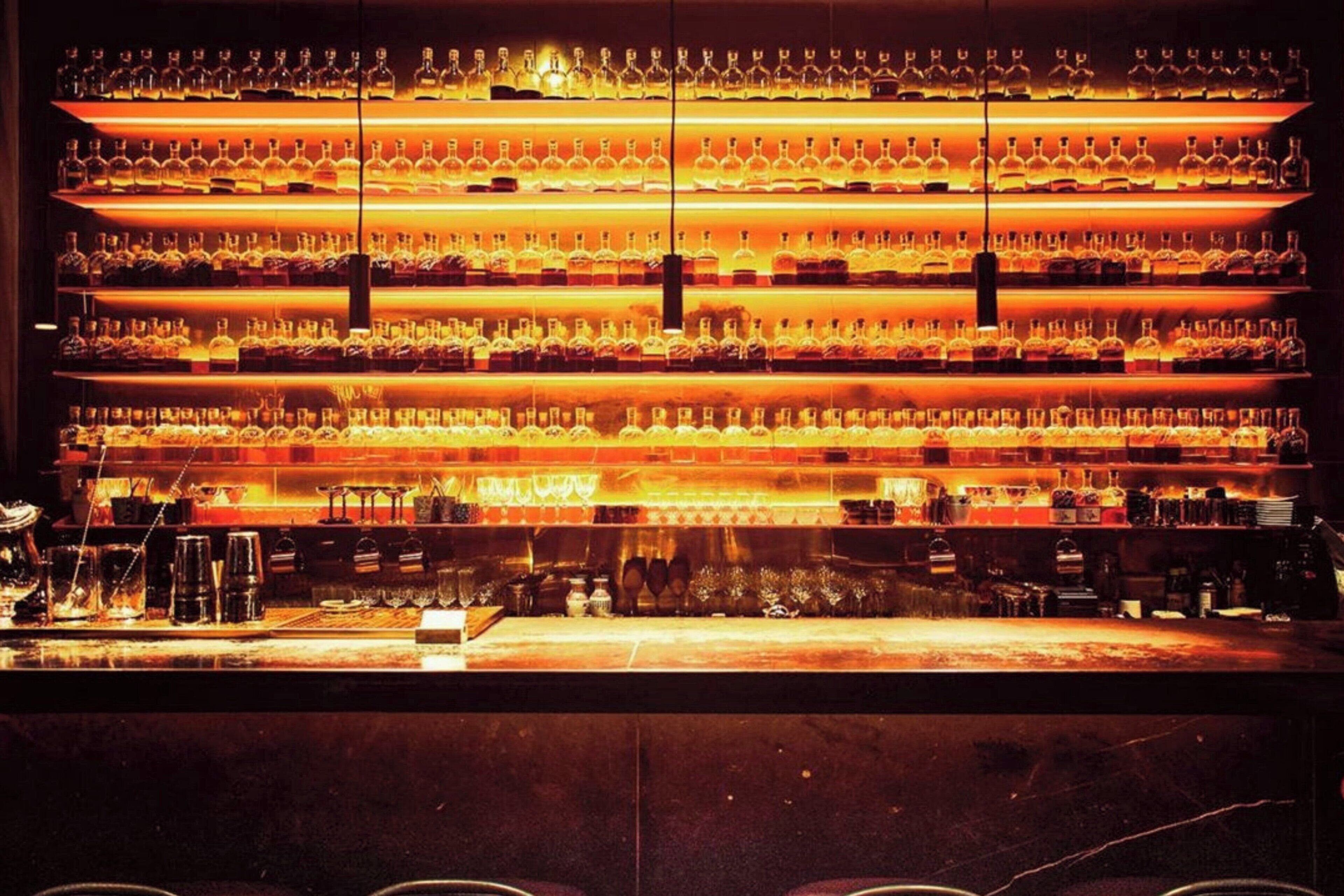 Un bar avec de nombreuses étagères remplies de bouteilles, un comptoir équipé d’ustensiles de bar et un sol sombre.