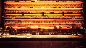 Un bar avec de nombreuses étagères remplies de bouteilles, un comptoir équipé d’ustensiles de bar et un sol sombre.