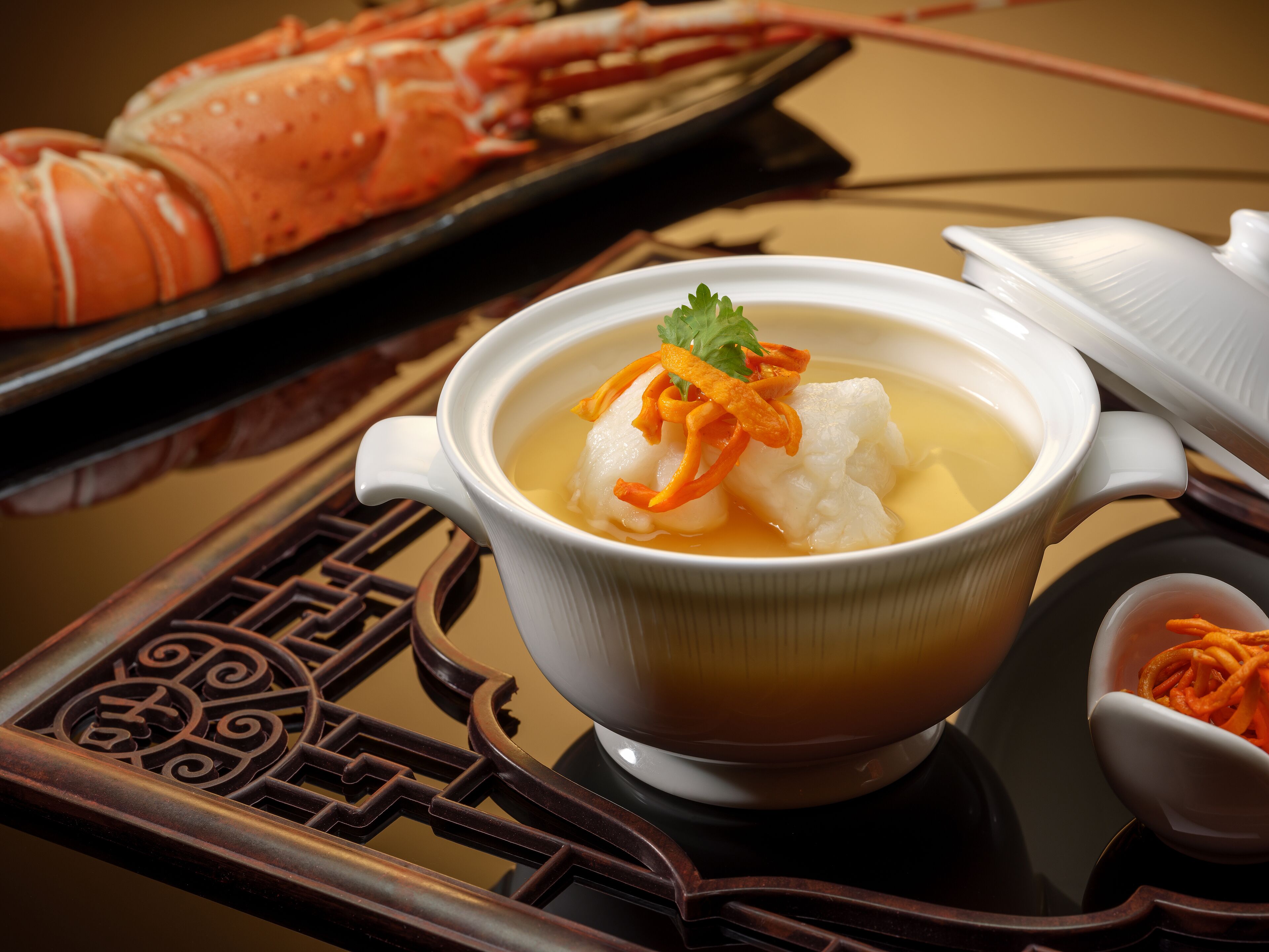 Un bol de soupe garni de poisson et de carottes, un plateau avec un homard et une théière.