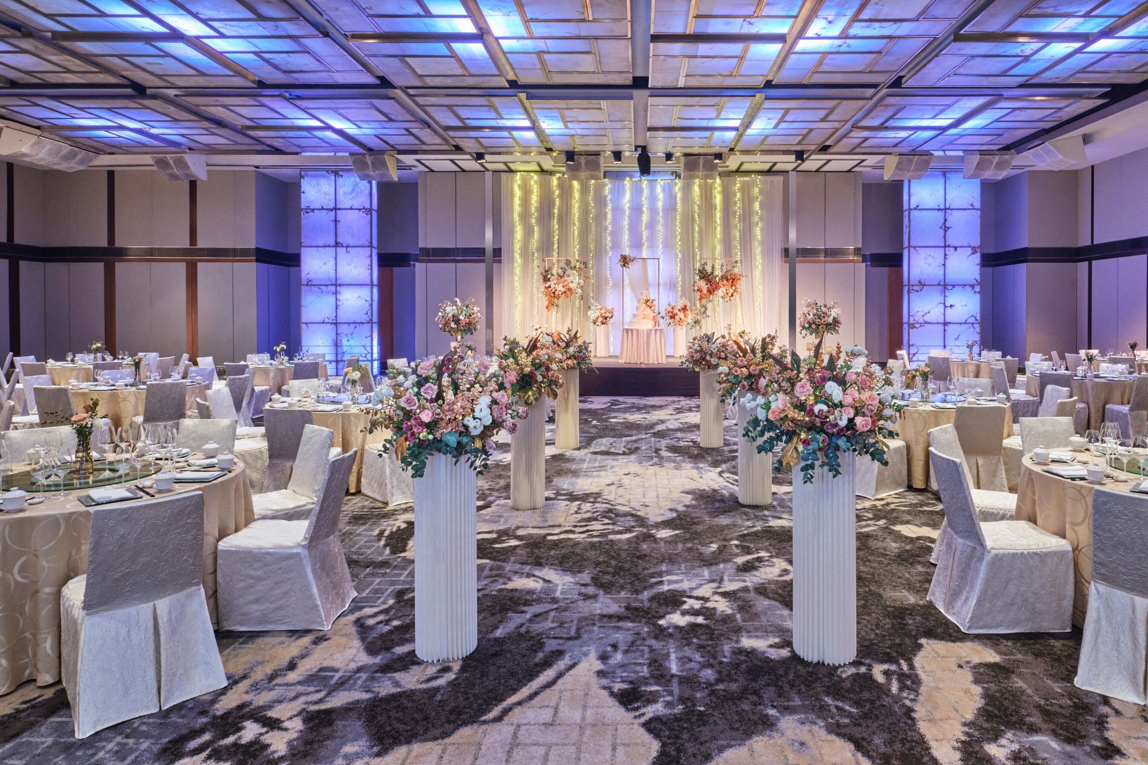 A banquet hall with round tables, white chairs, and floral centerpieces.