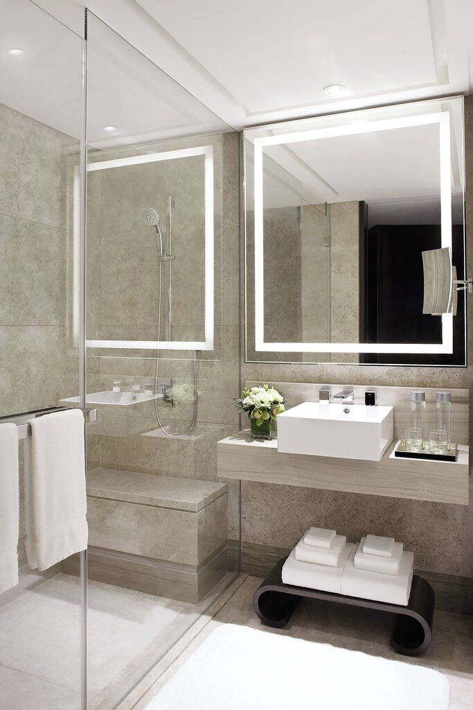 A modern bathroom with a glass shower enclosure, a large mirror, and a white sink with a vase of flowers.