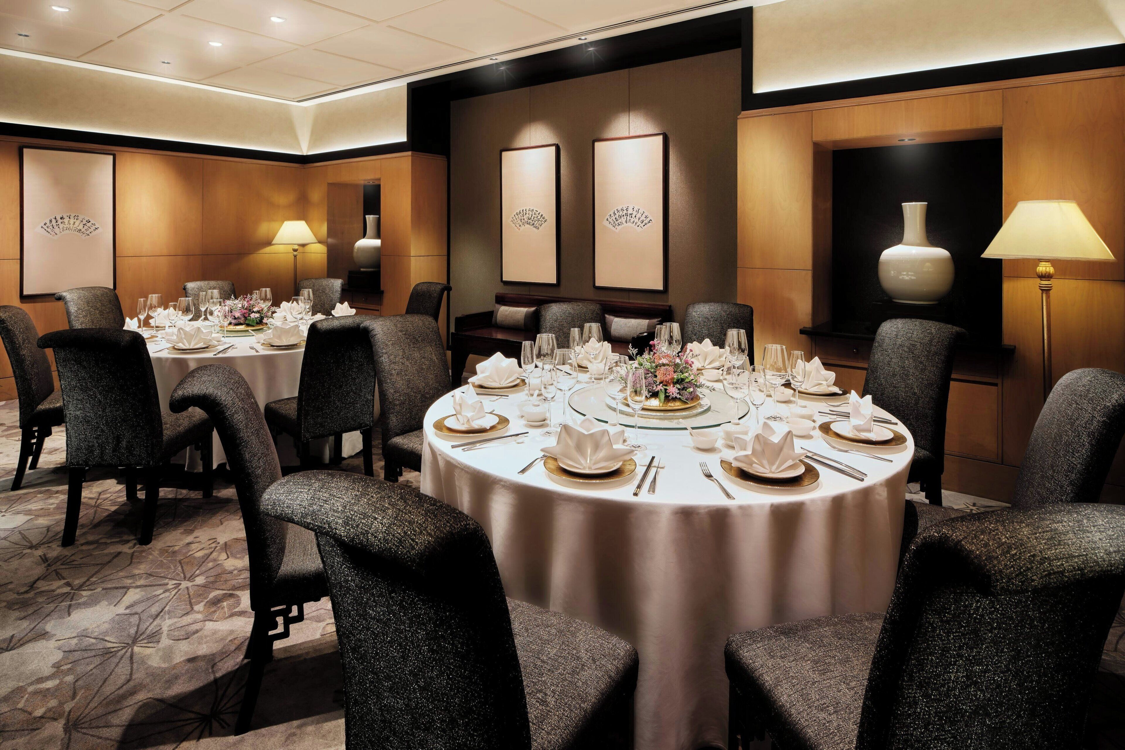 A banquet hall with round tables set for a formal event, featuring a carpeted floor and wall-mounted lamps.