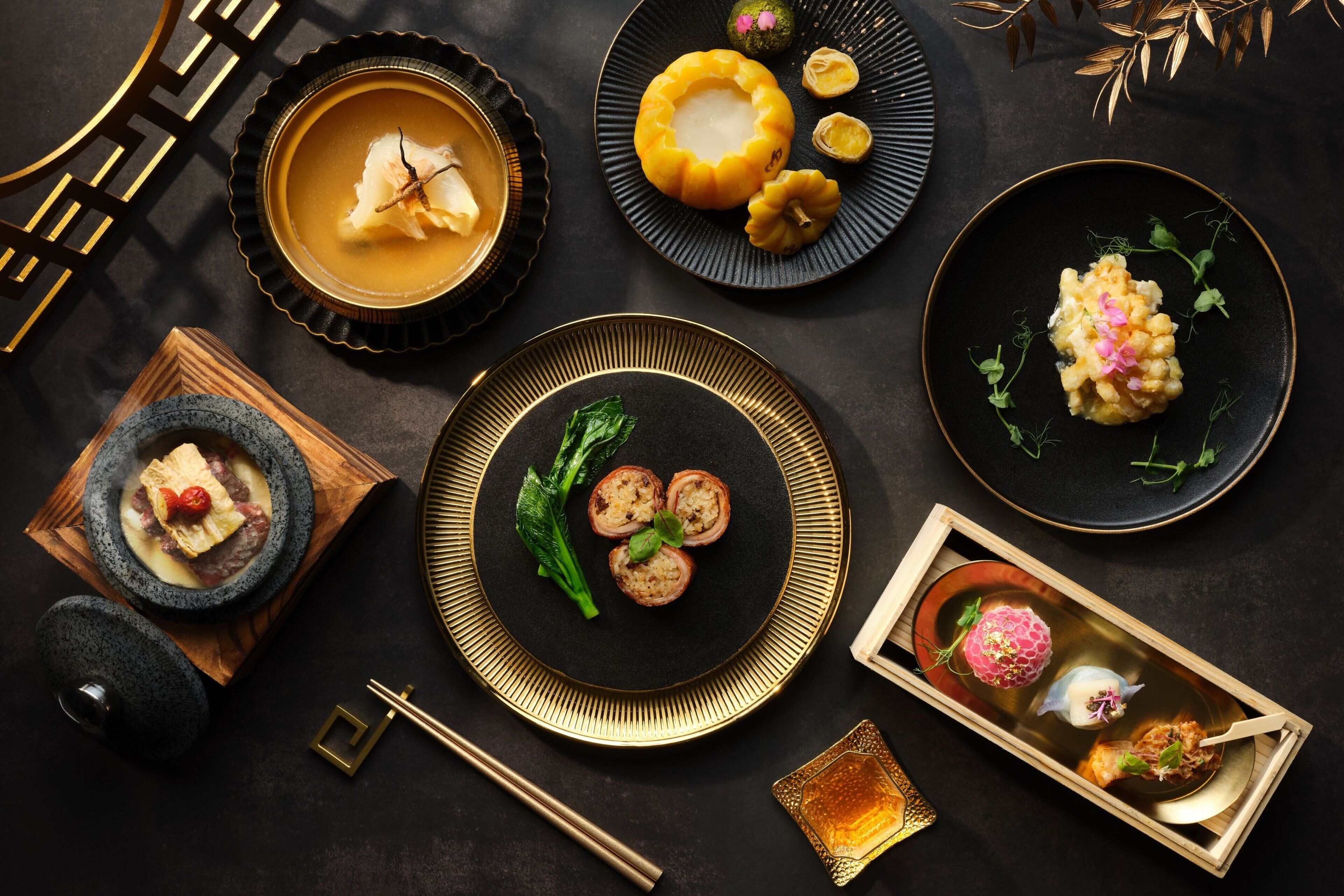 Forskellige retter på tallerkner, heriblandt en skål suppe, dumplings og en anretning med en dekorativ blomst.
