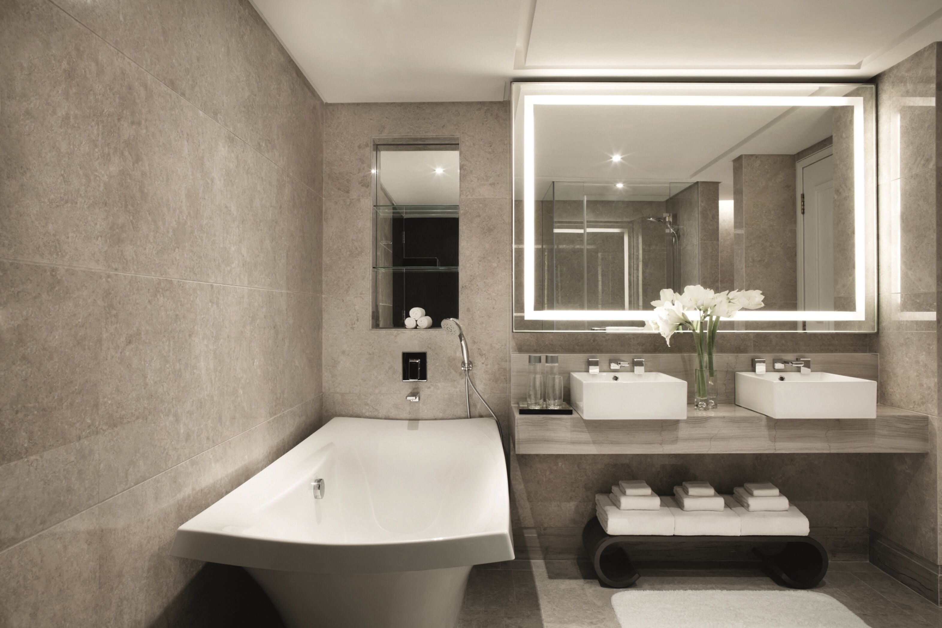 Une salle de bain moderne avec une baignoire sur pieds, deux vasques, un grand miroir et un banc avec des serviettes.