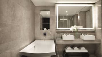 Une salle de bain moderne avec une baignoire sur pieds, deux vasques, un grand miroir et un banc avec des serviettes.