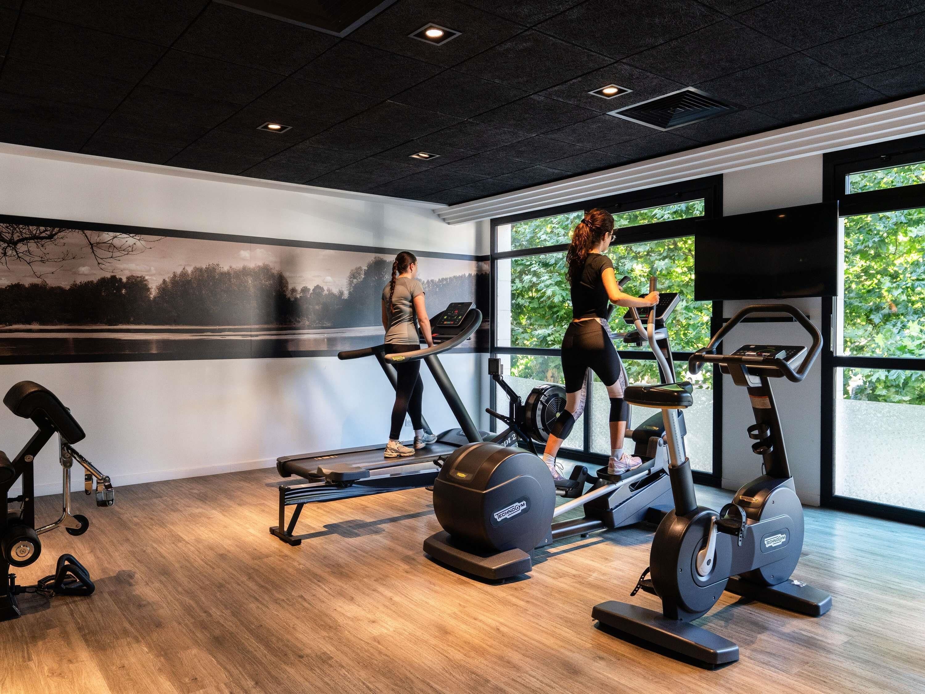 A gym with cardio equipment, a rowing machine, and a wall with a nature scene.