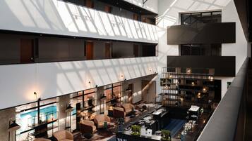 A multi-level hotel lobby with a bar area, seating, and a large glass ceiling allowing natural light.