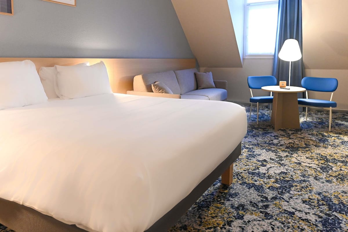 Una habitación de hotel con una cama grande, un sofá, dos sillas, una mesita y una lámpara.