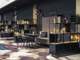 Un intérieur moderne avec un canapé, des fauteuils et une table, le tout entouré d’étagères et illuminé par des lampes suspendues.