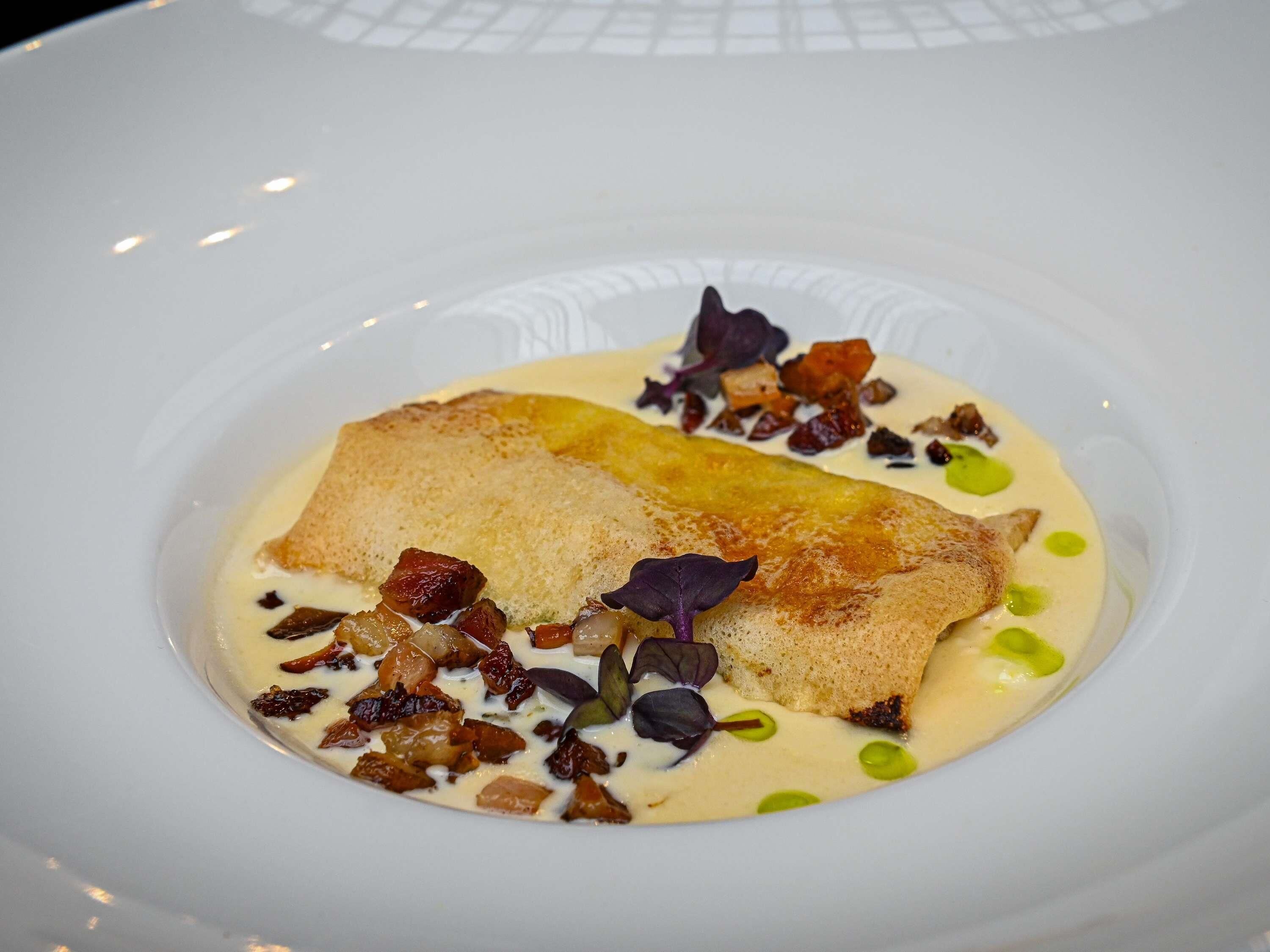 A white plate with a piece of fish, creamy sauce, and garnishes.