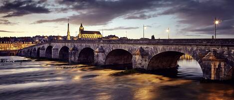 A stone bridge with multiple arches over a river, with buildings and a tower in the background.