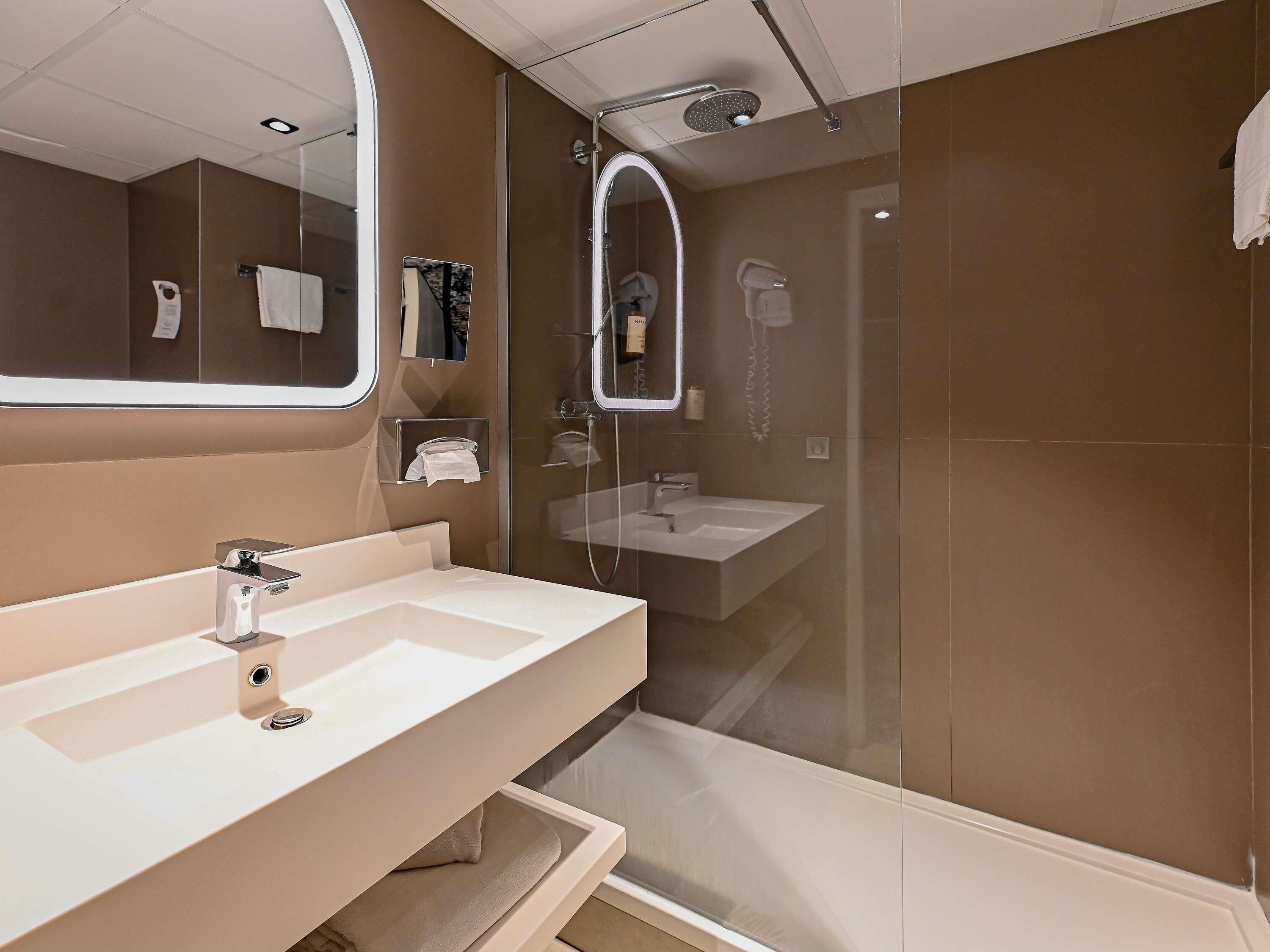 A modern bathroom with a large mirror, two sinks, a shower, and a glass-enclosed shower area.