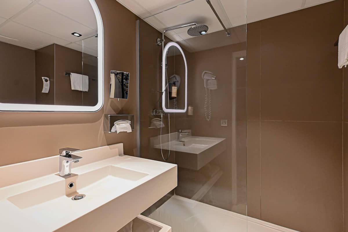 A modern bathroom with a large mirror, two sinks, a shower, and a glass-enclosed shower area.