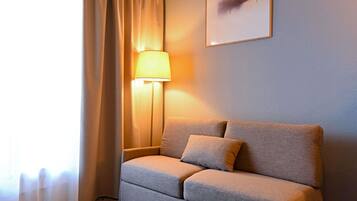 Quarto com sofá, luminária, janela com cortinas e uma obra de arte na parede.