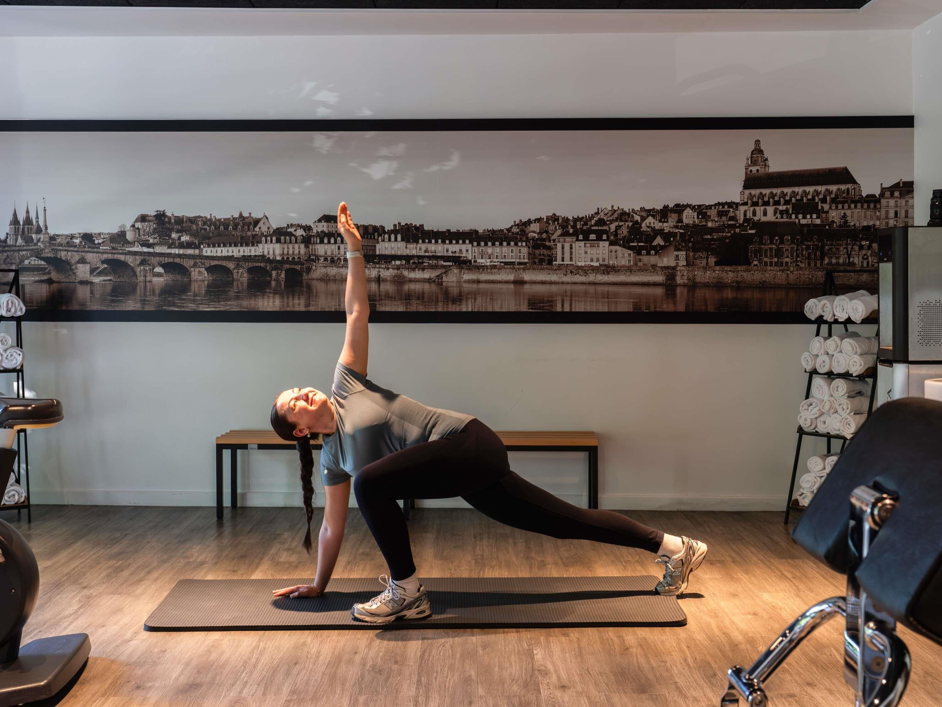A person performing a yoga pose on a mat in a room with a large cityscape mural on the wall.