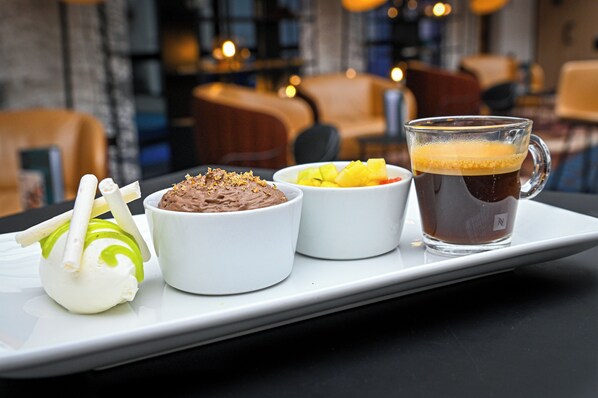 A tray with a dessert, a bowl of fruit, and a cup of coffee on a table in a restaurant.