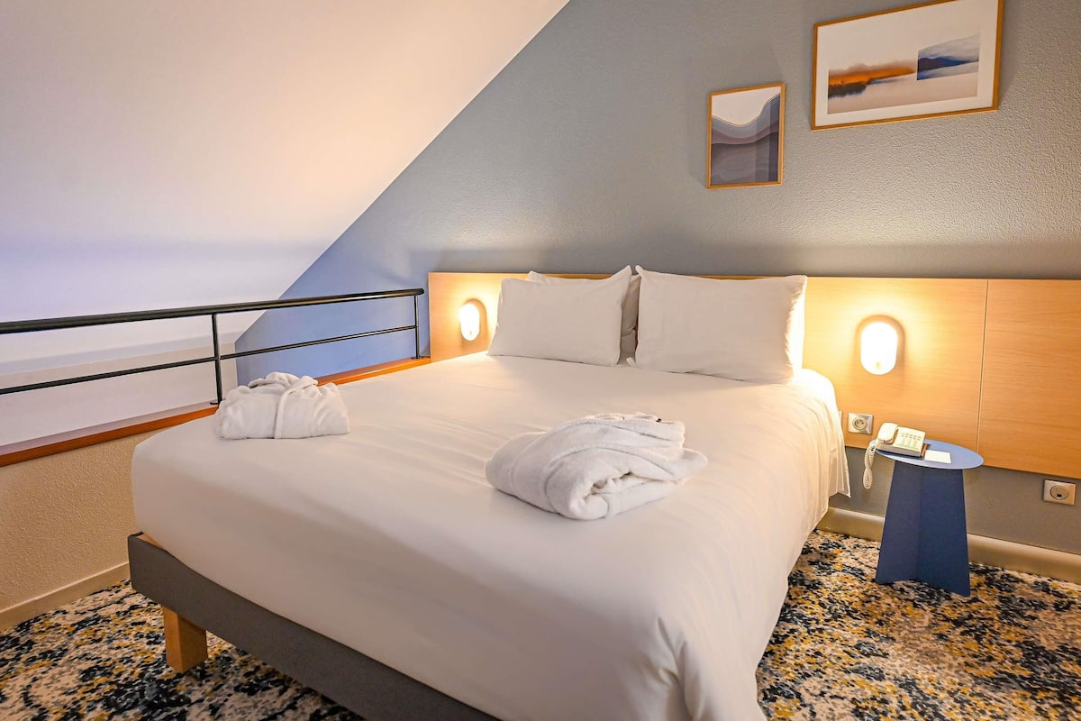 Habitación de hotel con cama, dos lámparas de noche, una mesita, teléfono y vista al mar.