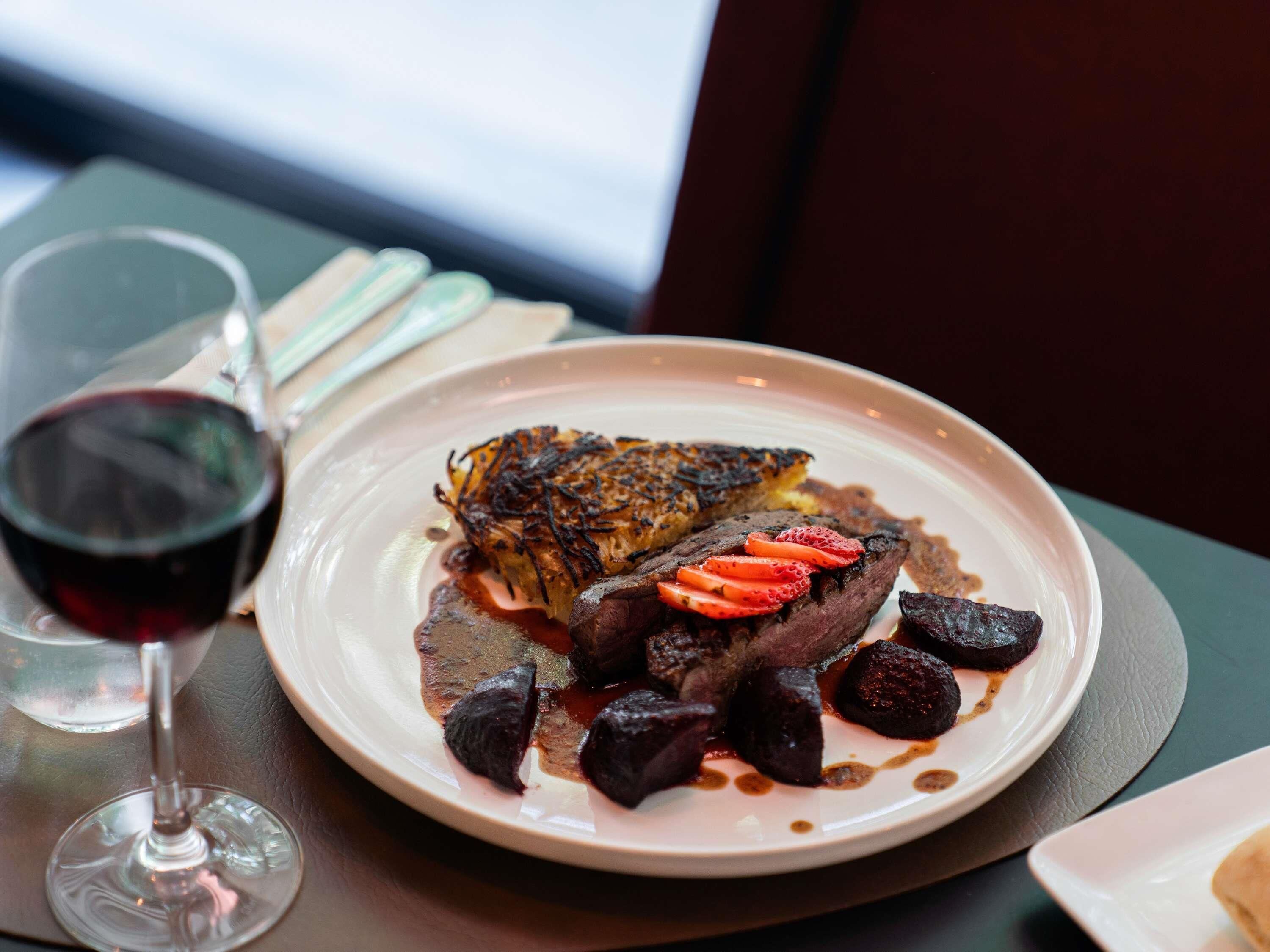 Une assiette garnie d’un steak, de pommes de terre rôties et d’une tranche de pain, accompagnée d’un verre de vin rouge.