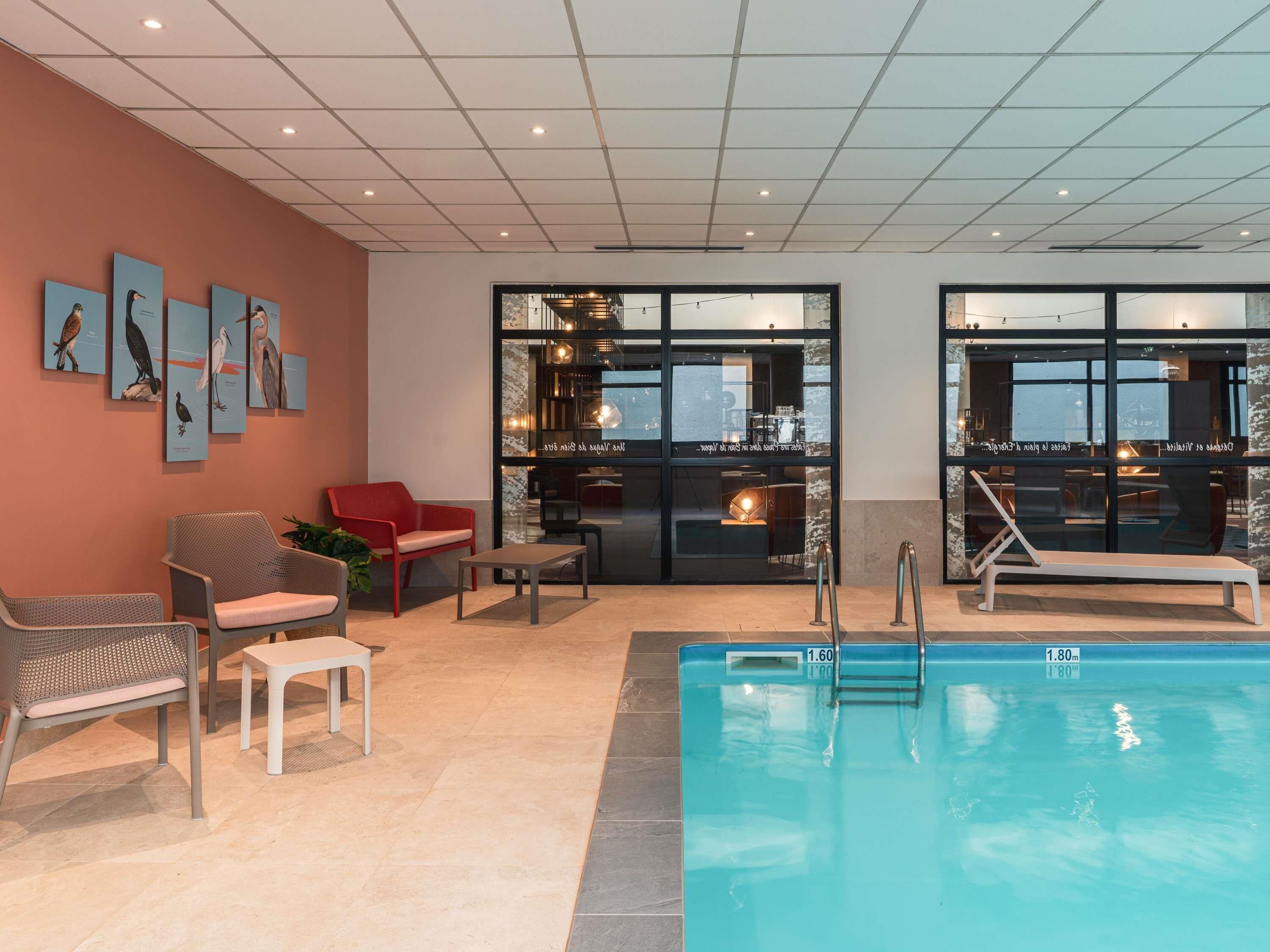 A modern indoor pool area with lounge chairs, a red sofa, and wall art.
