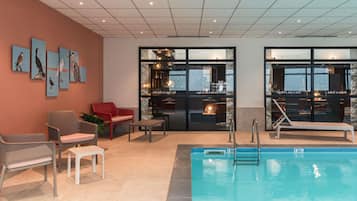 A modern indoor pool area with lounge chairs, a red sofa, and wall art.