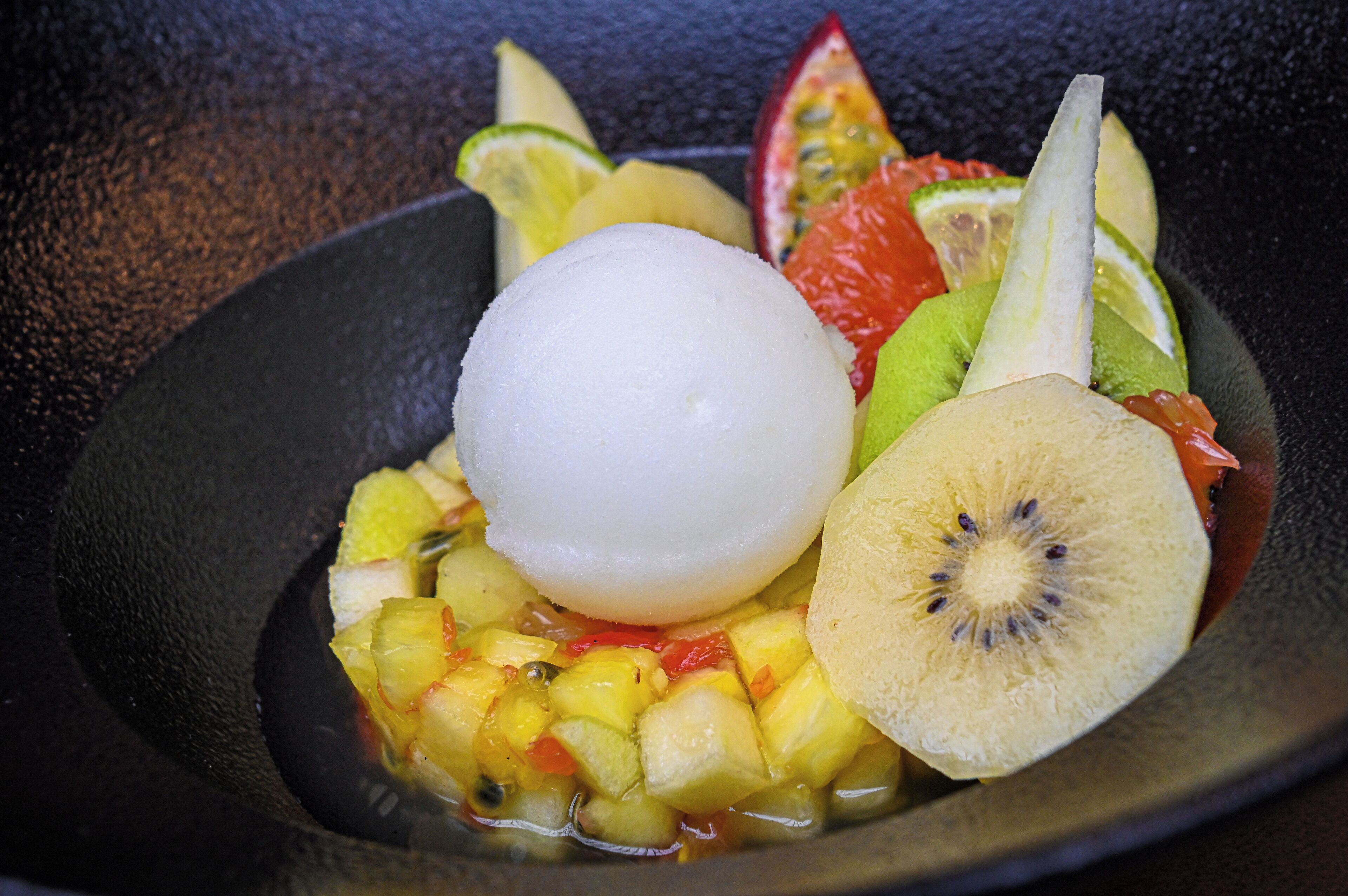 Un dessert composé d’une boule de glace et de différents fruits.