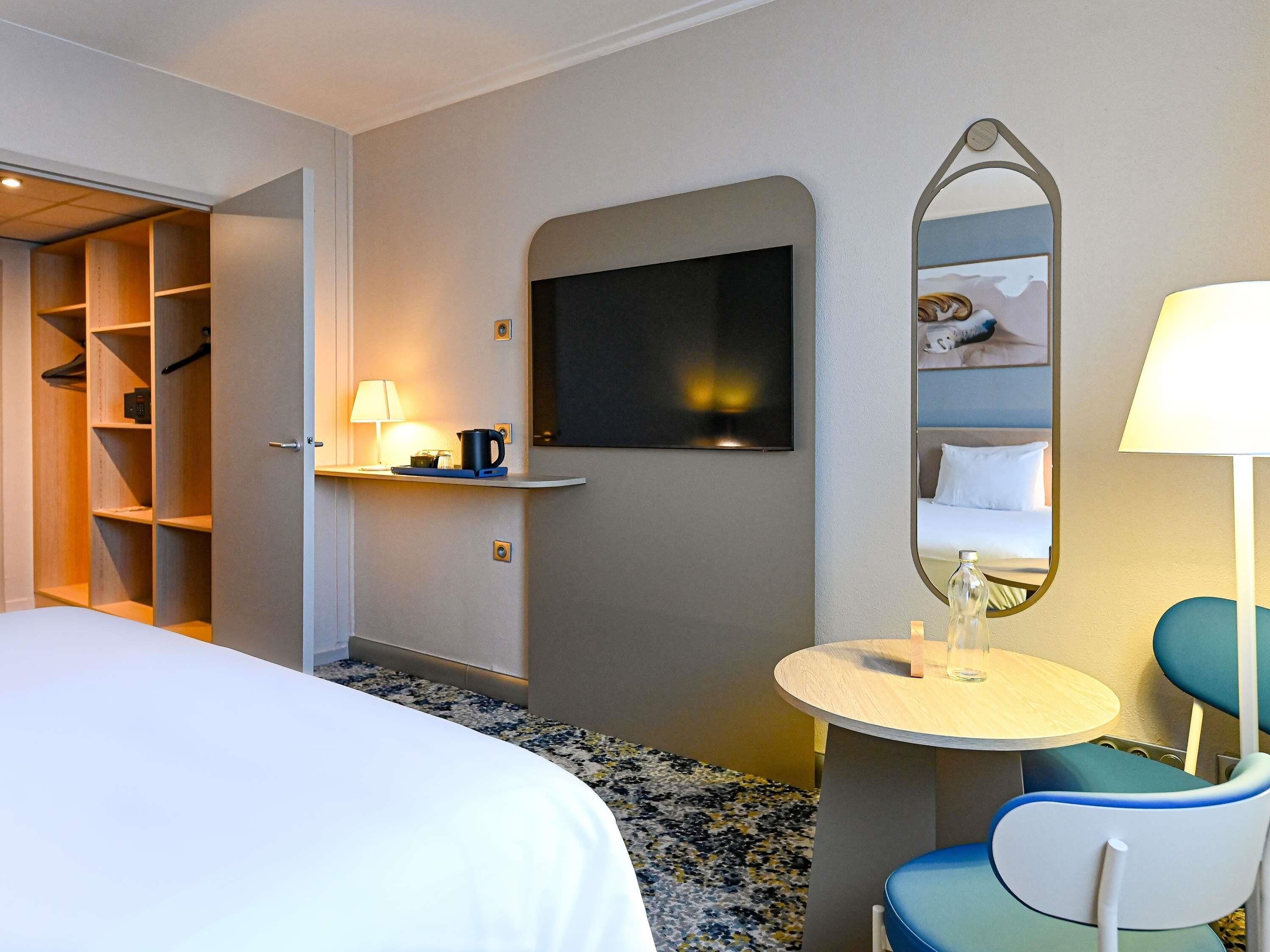 A hotel room with a bed, a desk with a lamp, a mirror, and a chair.