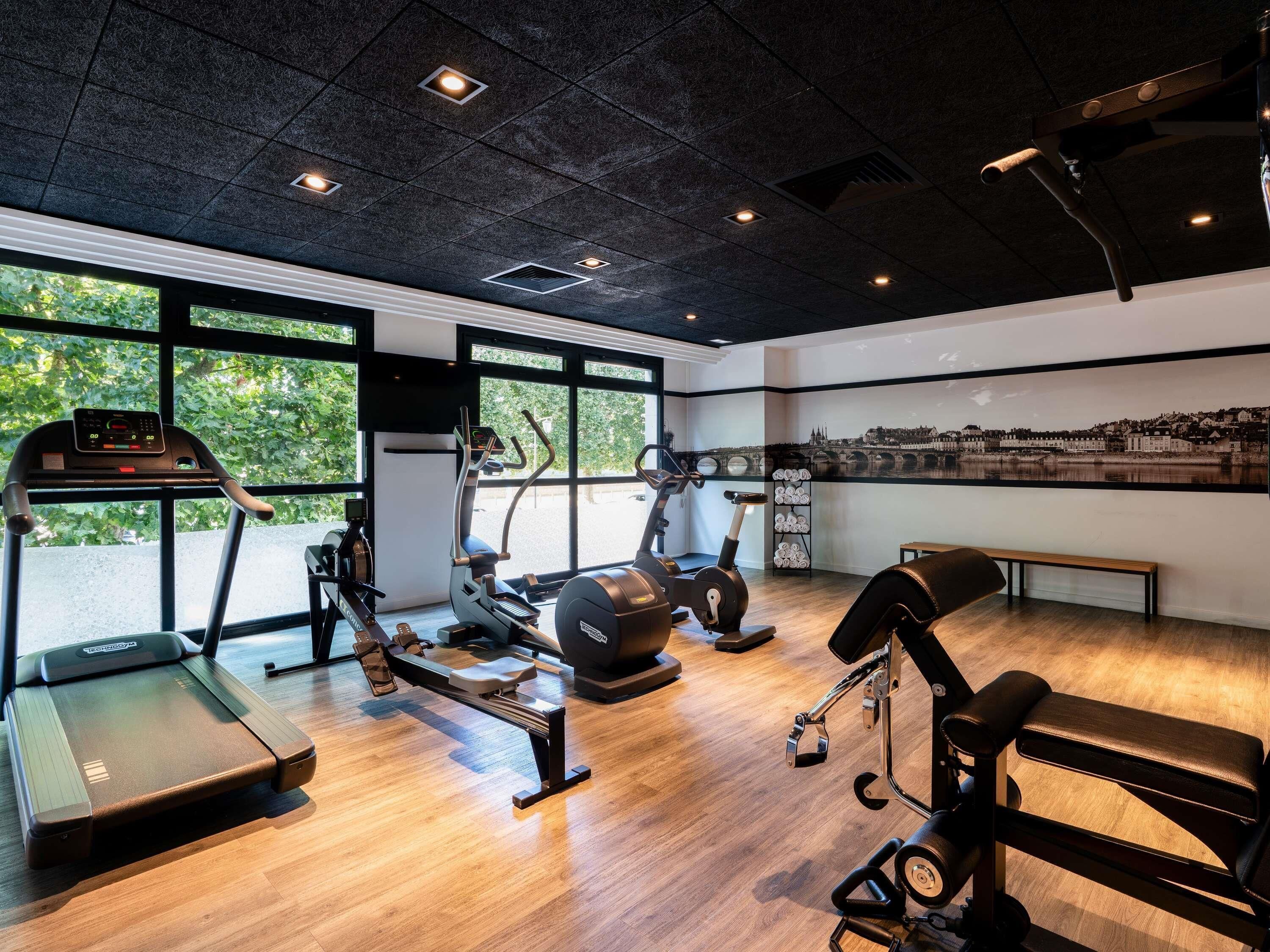 Un gimnasio con máquinas de cardio, una máquina de remo y una banca.