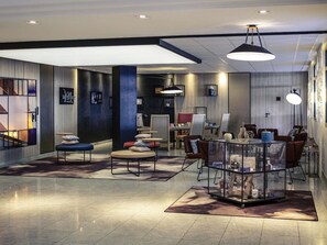 Un hall d’hôtel moderne doté d’un espace salon central, d’un comptoir d’accueil et d’une grande fenêtre laissant entrer la lumière naturelle.