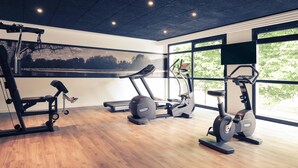 Een sportschool met cardioapparatuur, gewichthefapparatuur en grote ramen die natuurlijk licht en uitzicht op bomen bieden.