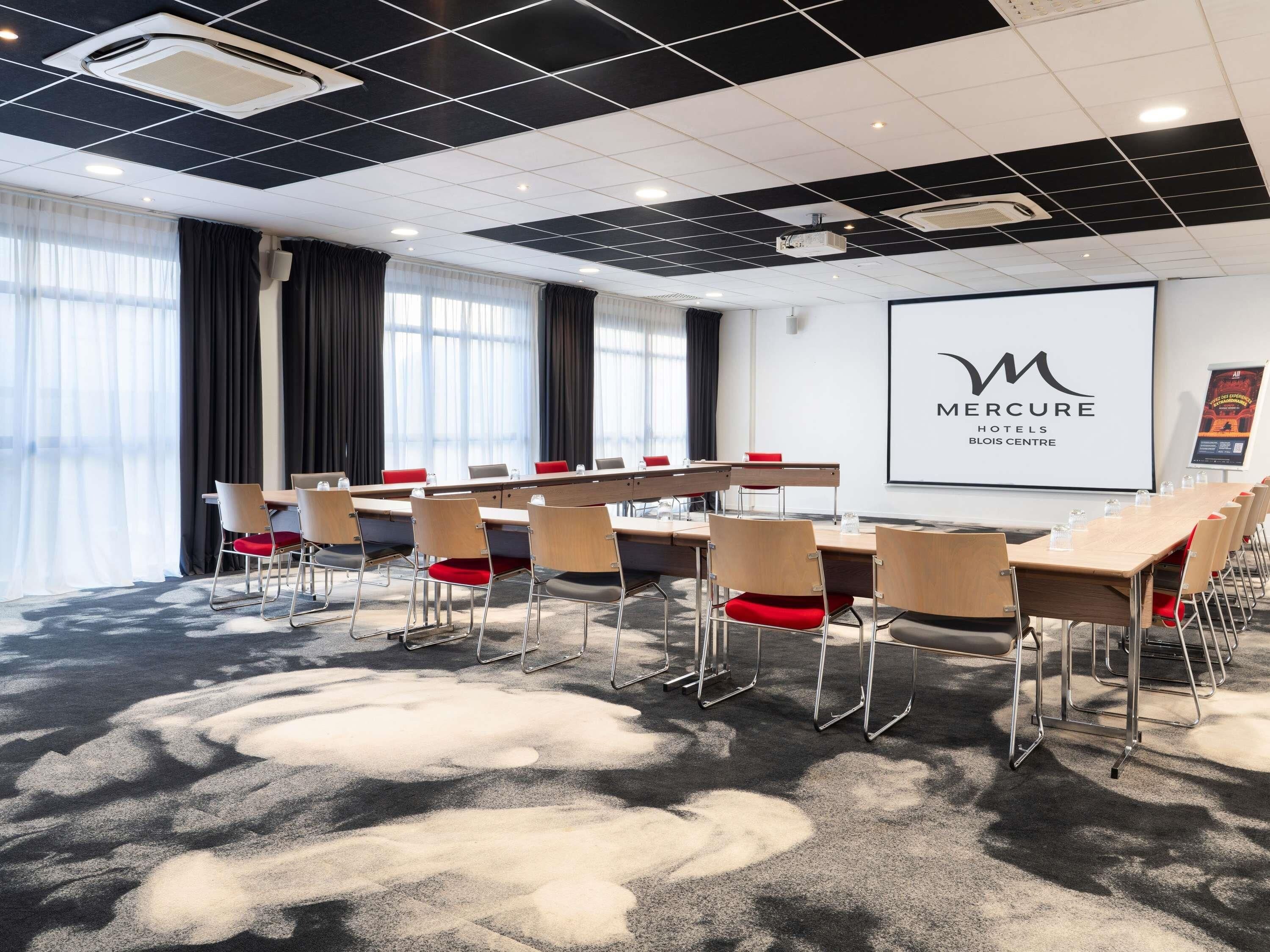 Un salón de conferencias con una larga mesa, sillas y una pantalla de proyector.