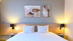 Habitación de hotel con una cama grande, dos lámparas de noche, un teléfono y dos cuadros en la pared.