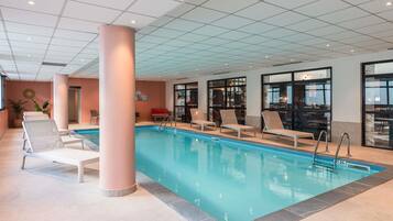 An indoor swimming pool with lounge chairs and a large pillar.