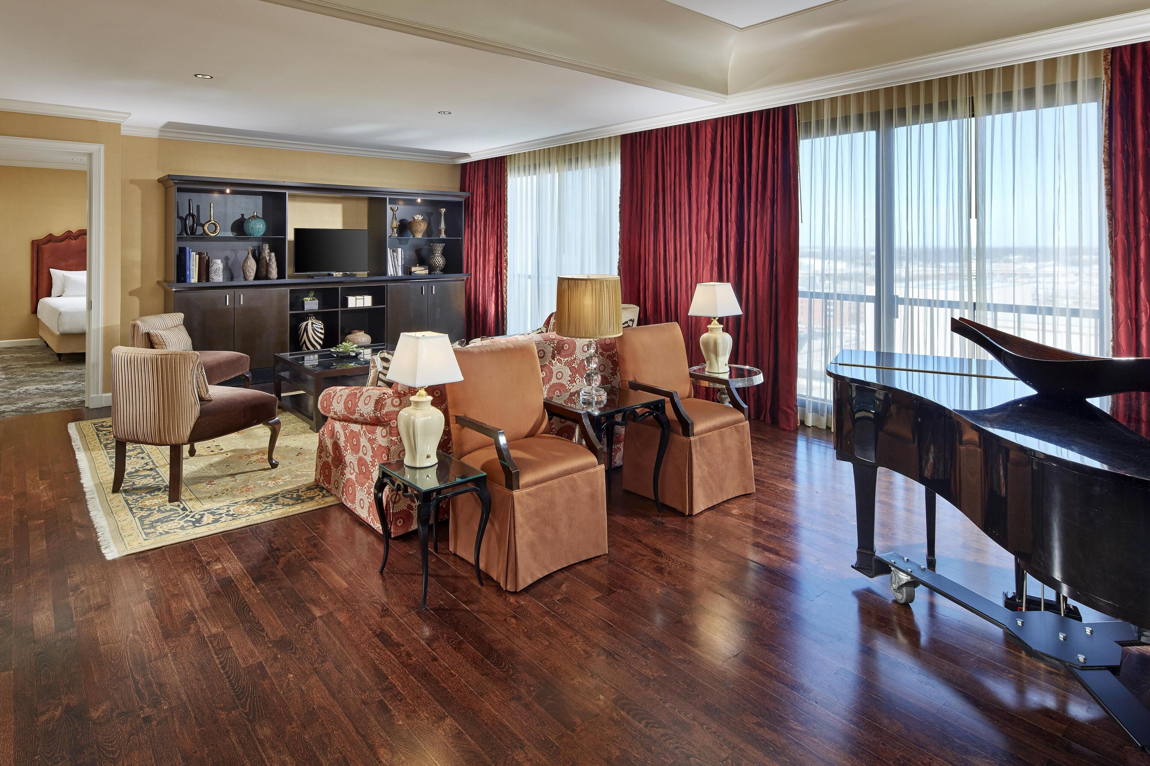 A spacious living room with a grand piano, comfortable seating, a television, and a large window with curtains.