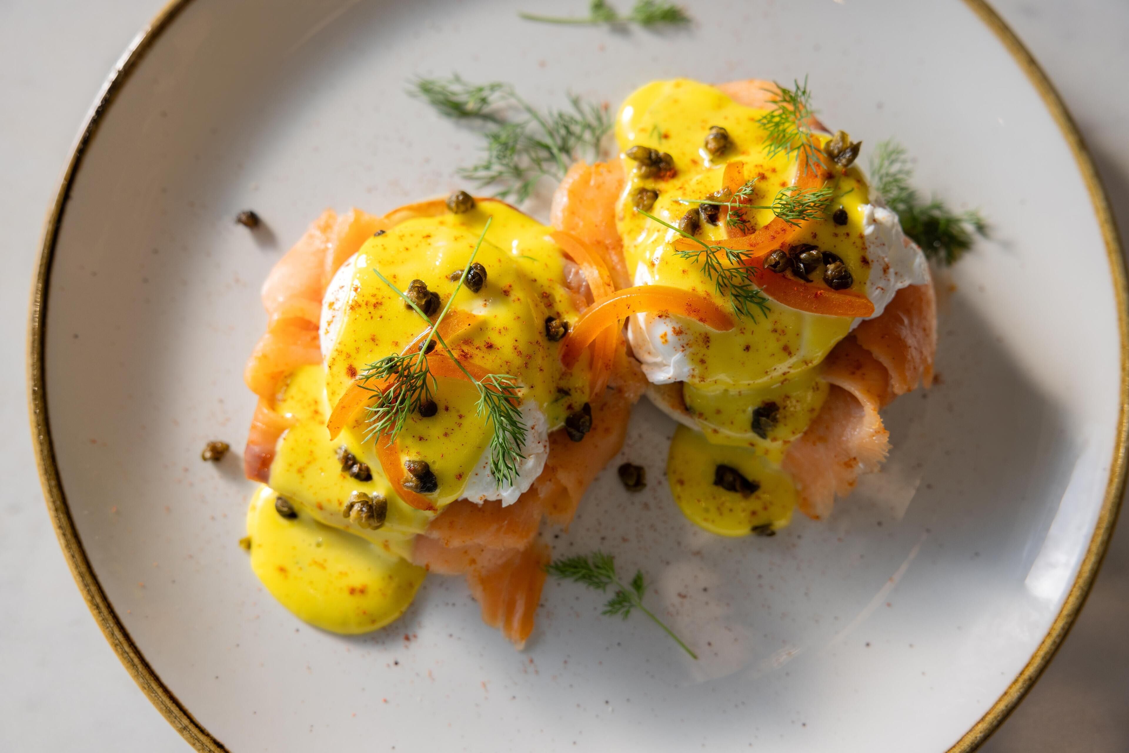 Un plato con dos trozos de salmón cubiertos de salsa holandesa y adornados con alcaparras y eneldo.