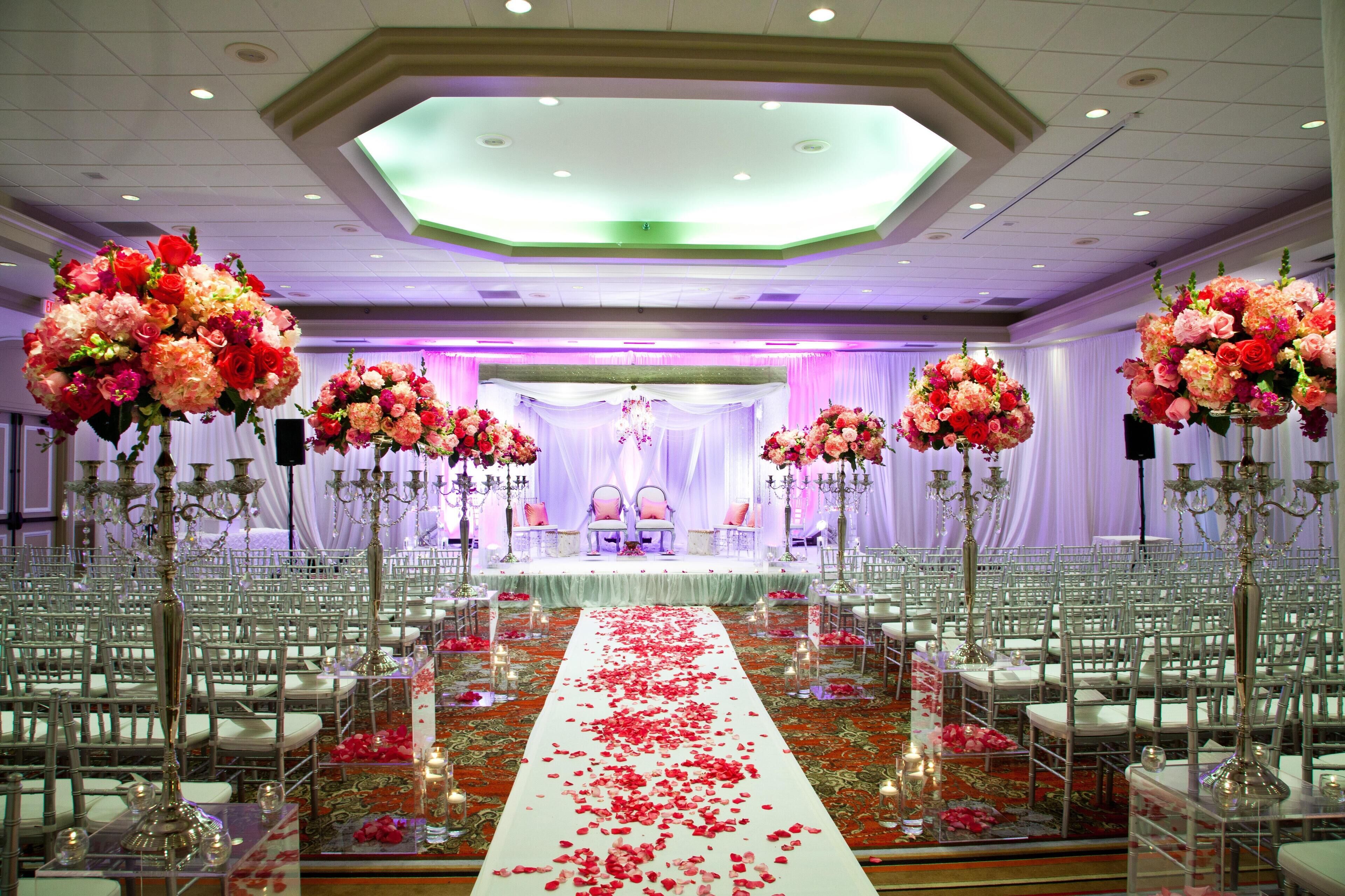 A wedding venue with rows of white chairs, a central aisle with rose petals, and large floral arrangements.