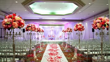 A wedding venue with rows of white chairs, a central aisle with rose petals, and large floral arrangements.