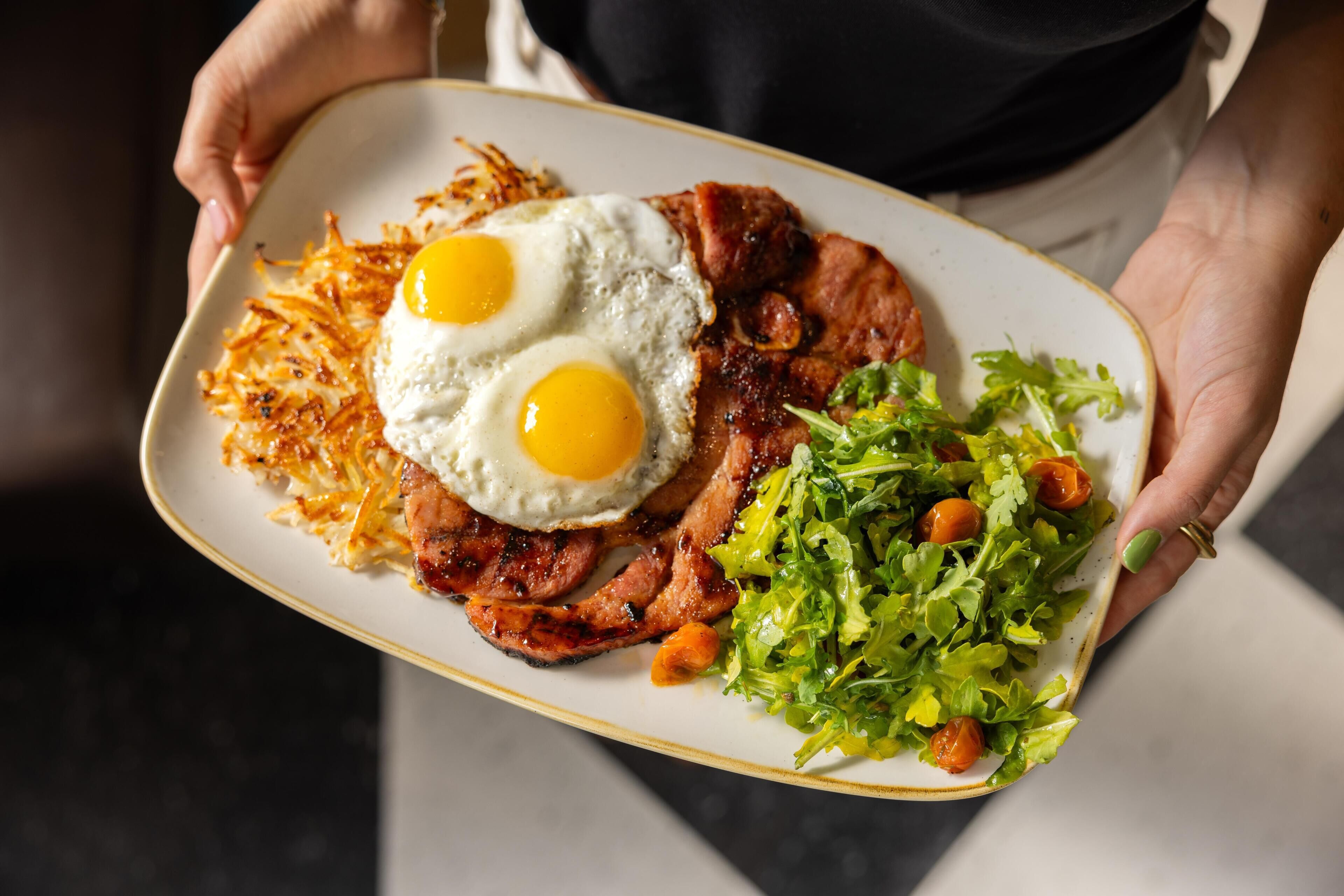 A person holding a plate with eggs, bacon, hash browns, and a salad.