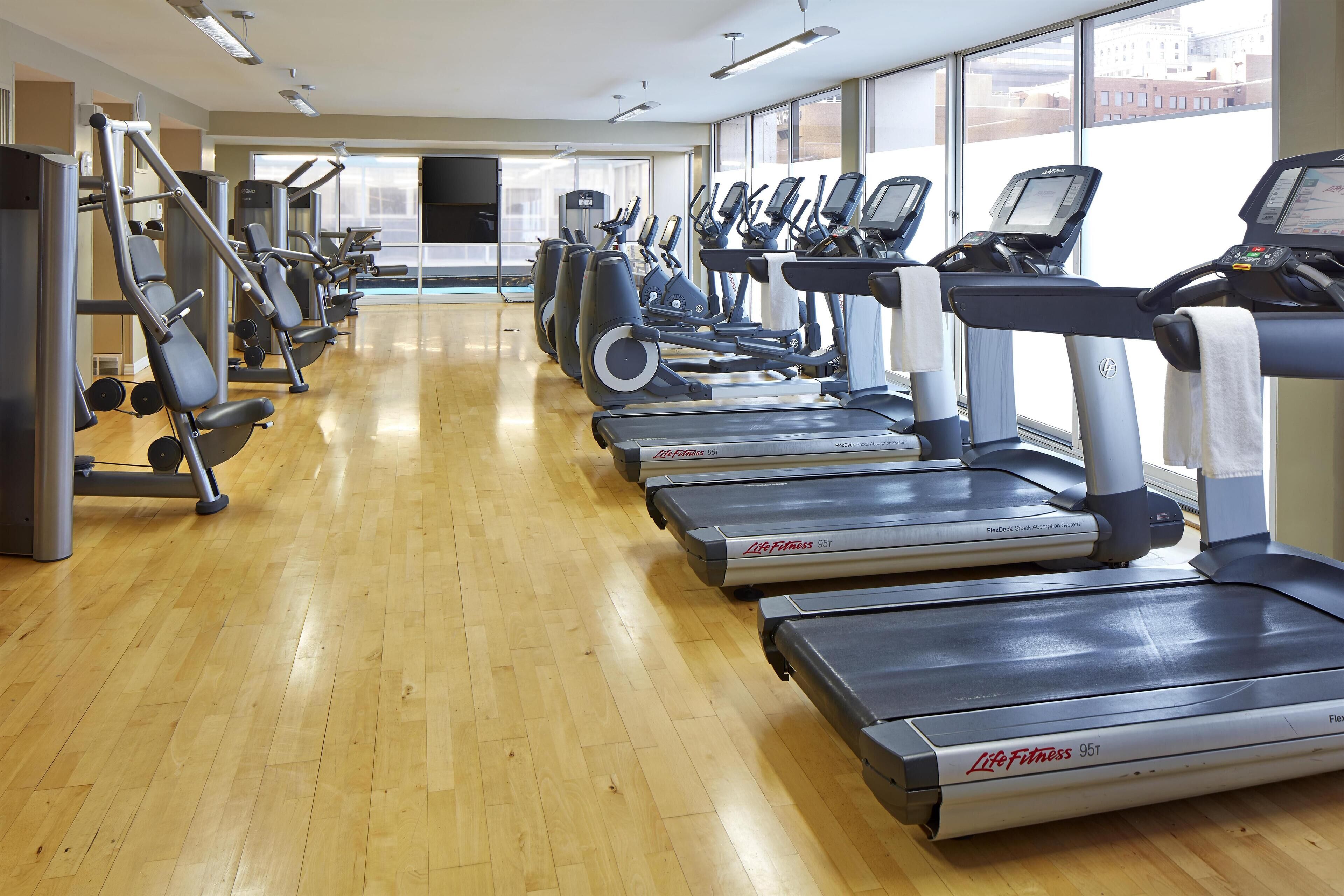 Une salle de sport équipée de plusieurs tapis de course, de machines de musculation et dotée d’un plancher en bois.