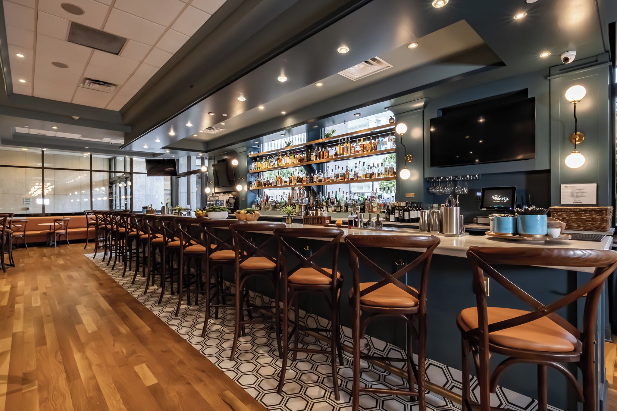 A bar area with wooden flooring, bar stools, and shelves stocked with bottles.