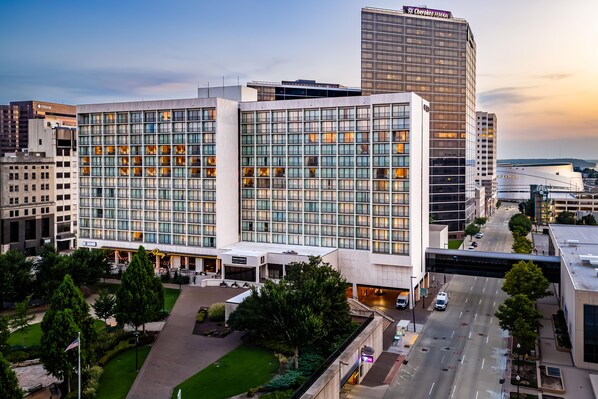 A modern hotel with a glass facade, a parking garage, and a view of the cityscape.