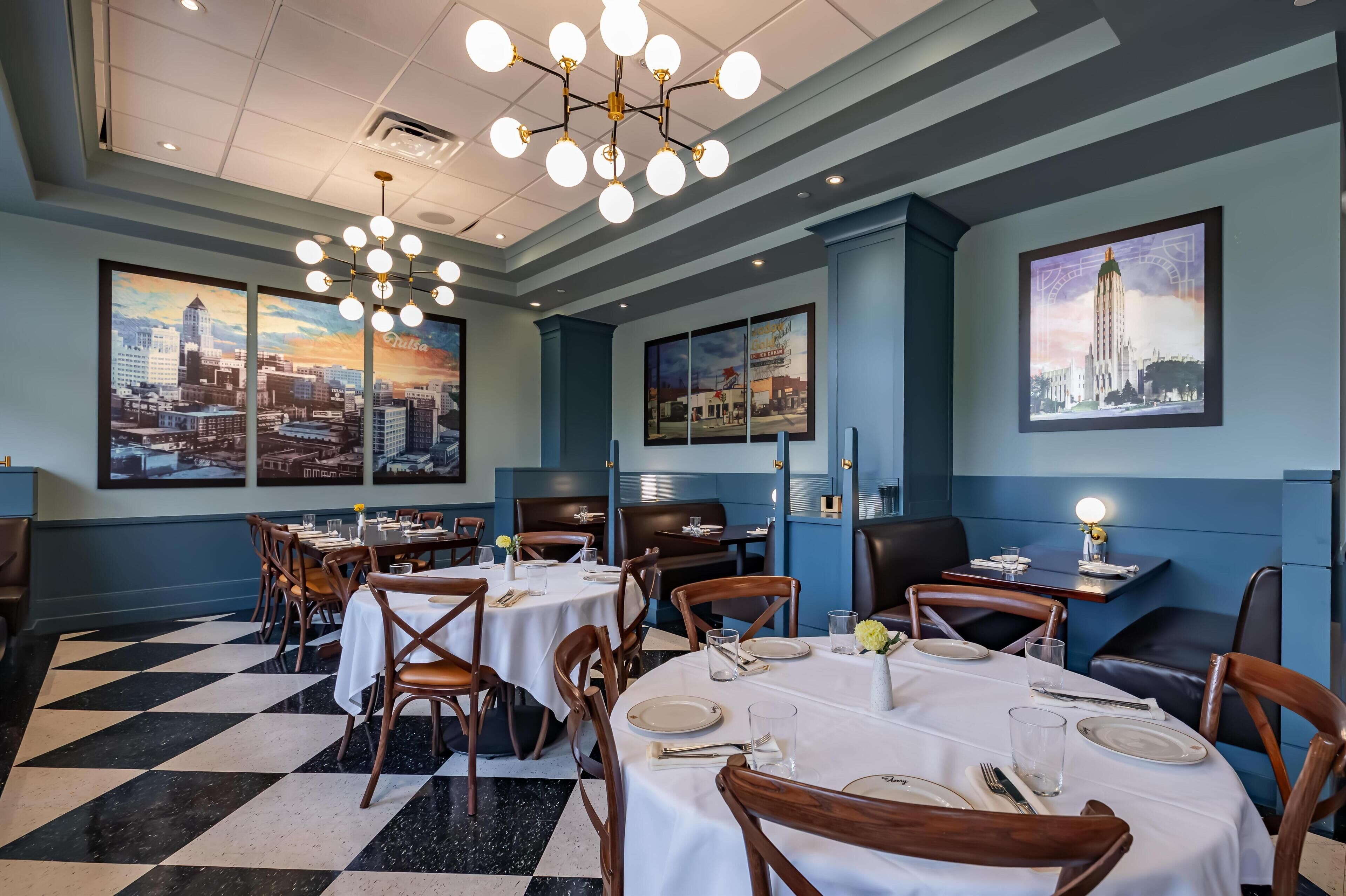 Un restaurant avec des tables rondes, des chaises et des tableaux représentant des vues de la ville, accrochés aux murs.