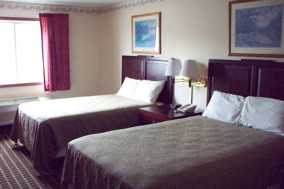 A hotel room with two beds, a nightstand with a lamp, a telephone, and a window with curtains.