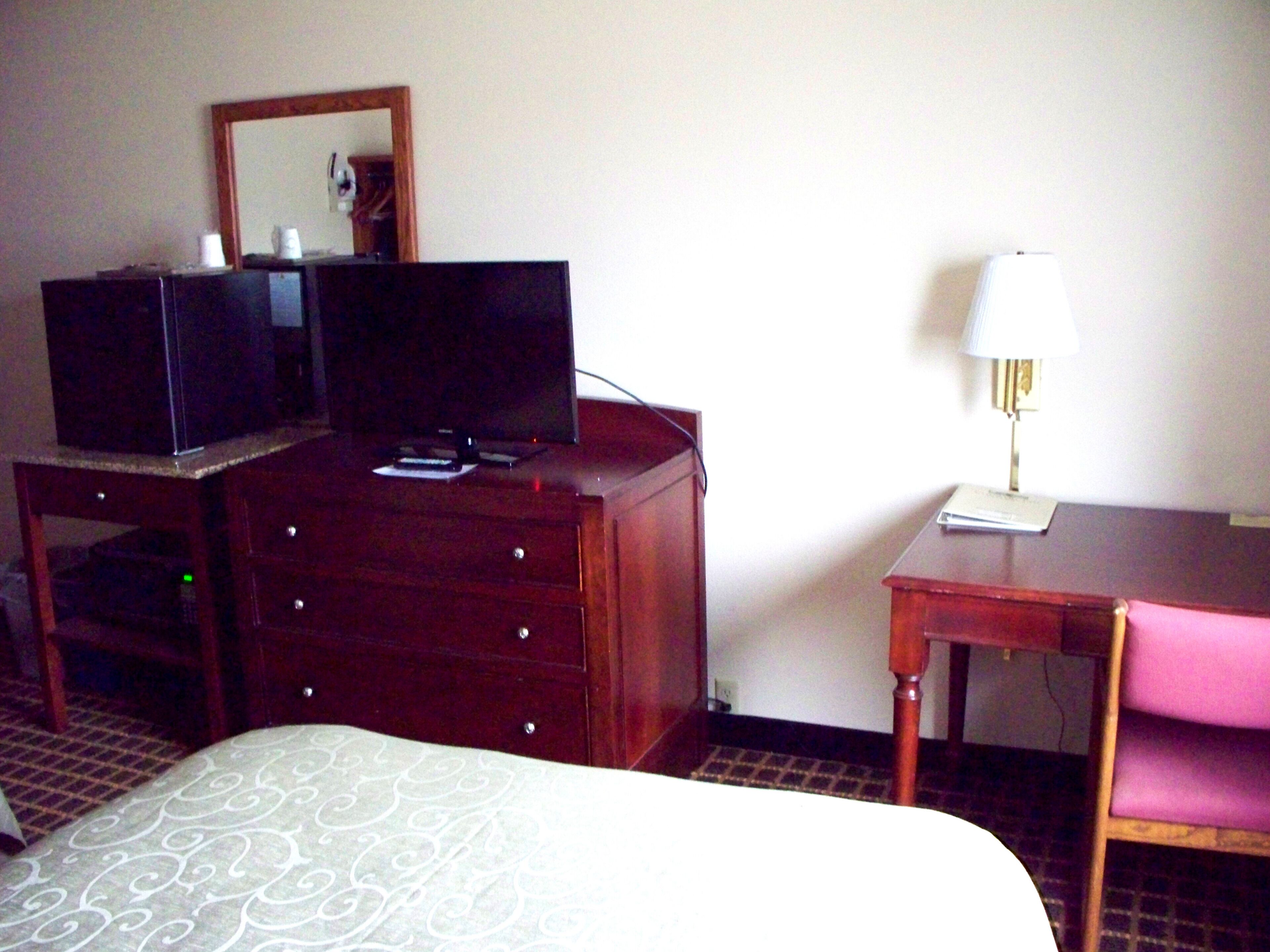 Une chambre d’hôtel comprenant un lit, une commode en bois avec un téléviseur, un bureau avec une lampe et une chaise.
