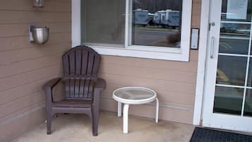 Een hoekje met een bruine Adirondack stoel, een witte bijzettafeltje en een raam met uitzicht op campers op de achtergrond.