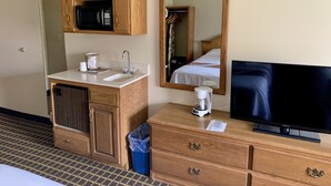 A hotel room with a wooden cabinet containing a microwave, a sink, and a coffee maker. There is a mirror on the wall, a television, and a trash bin. - Country Inn Deerwood (Deerwood)